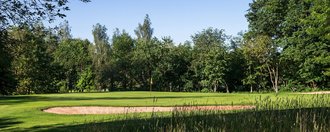 Unspielbares Gelände und Bäume vor einem Bunker und dem Grün der Golfbahn 16 auf der Golfanlage Allgäuer Golf- und Landclub e.V. Ottobeuren