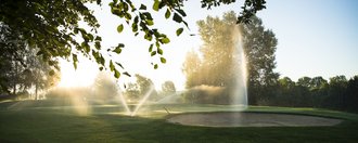 Wassersprenger bewässern in spektakulären Fontänen eine Bahn inklusive Bunker auf dem Golfplatz des Allgäuer Golf- und Landclub e.V. vor dem gegenlicht der untergehenden Sonne (Credit: Stefan von Stengel)