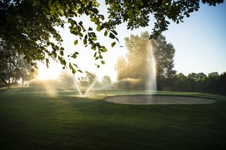 Wassersprenger bewässern in spektakulären Fontänen eine Bahn inklusive Bunker auf dem Golfplatz des Allgäuer Golf- und Landclub e.V. vor dem gegenlicht der untergehenden Sonne (Credit: Stefan von Stengel)