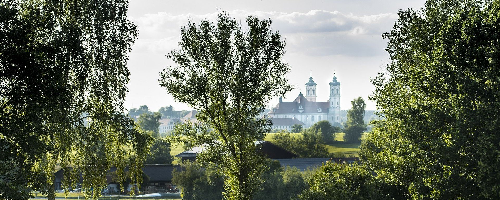 Ein Golferpaar läuft über das gepflegte Green des Golfanlage des Allgäuer Golf- und Landclub e.V. – im Hintergrund ragt die Basilika Ottobeuren hinter den Bäumen hervor (Credit: Stefan von Stengel)