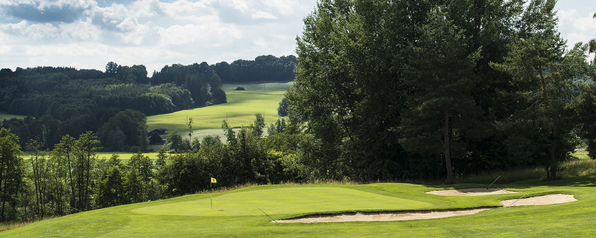 Das Loch 6 auf dem Golfplatz des Allgäuer Golf- und Landclub e.V. mit sanften Hügeln, Bäumen und Buschwerk im Hintergrund (Credit: Stefan von Stengel)