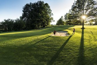 Zwei Golfer auf dem Golfplatz des Allgäuer Golf- und Landclub e.V., von denen einer einen Bunkerschlag in einem Sandbunker nahe des Lochs ausführt. (Credit: Stefan von Stengel)