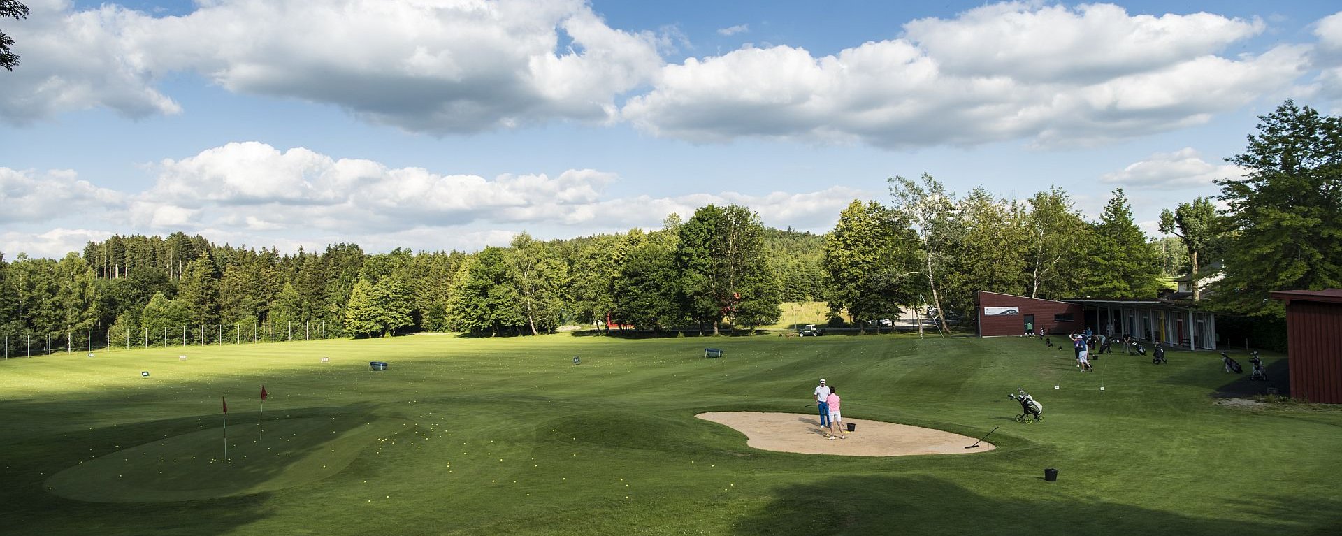 Die Driving-Range des Allgäuer Golf- und Landclub e.V. mit vielen Golfern in den Schlaghäuschen und vielen auf dem Green verteilten Golfbällen