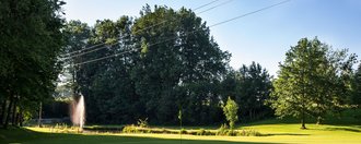 Ein Teich mit Wasserspiel und das Grün der Golfbahn 17 auf der Golfanlage Allgäuer Golf- und Landclub e.V. Ottobeuren